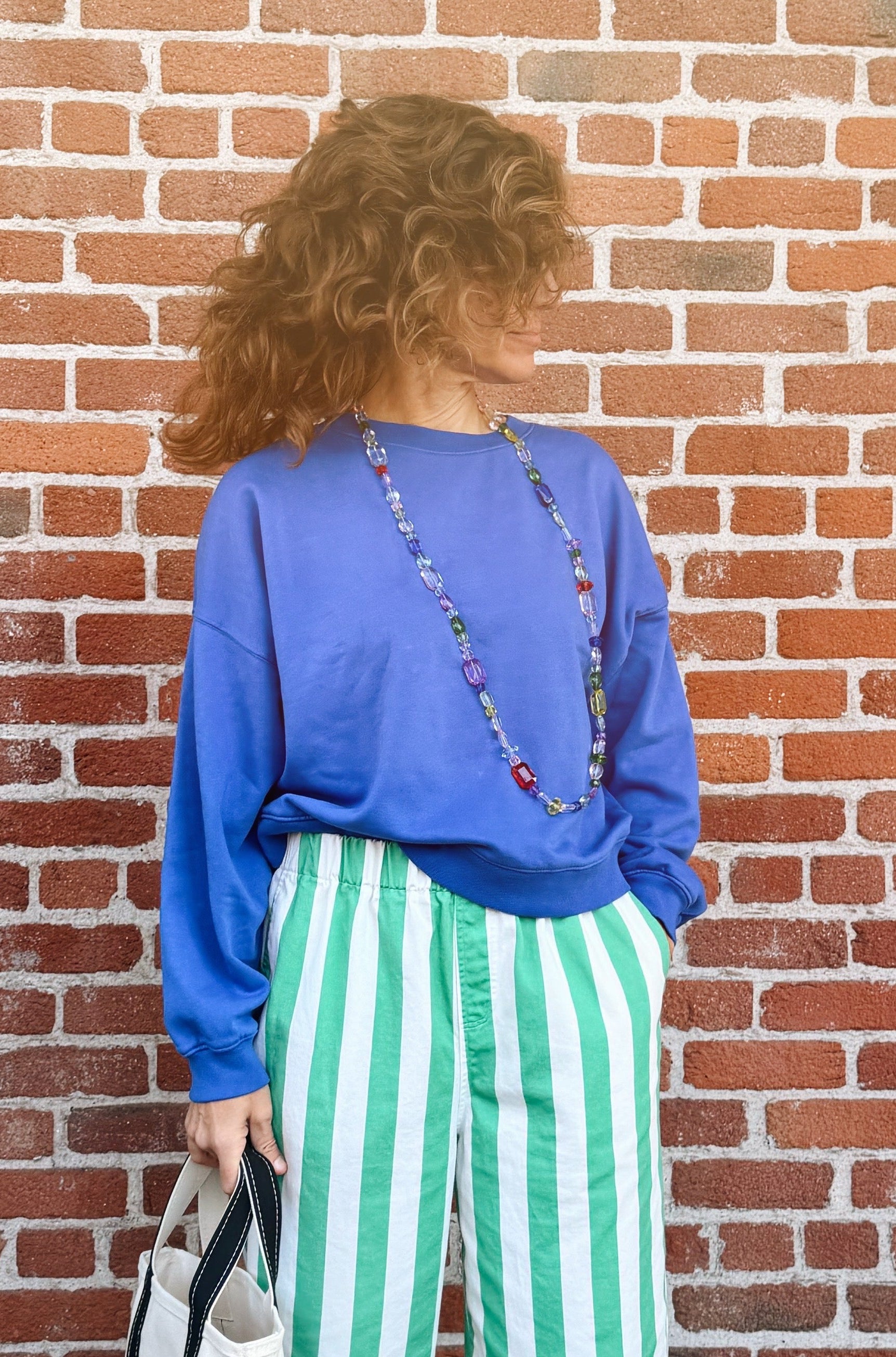 Person wearing a blue shirt and green striped pants standing against a brick wall.