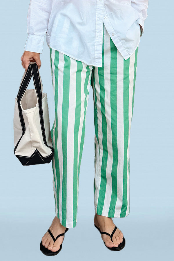 Person wearing green and white striped pants holding a tote bag against a light blue background
